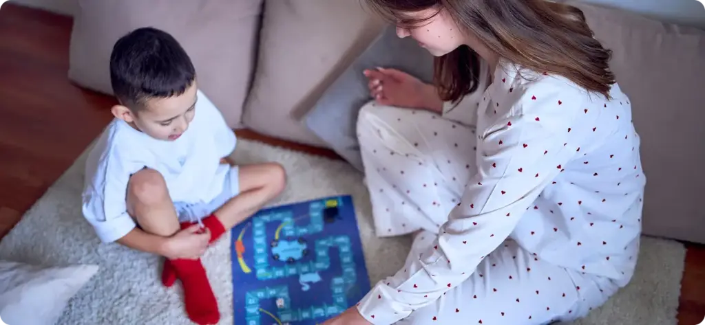 Moeder en zoon zitten in pyjama's op bed en spelen een bordspel.