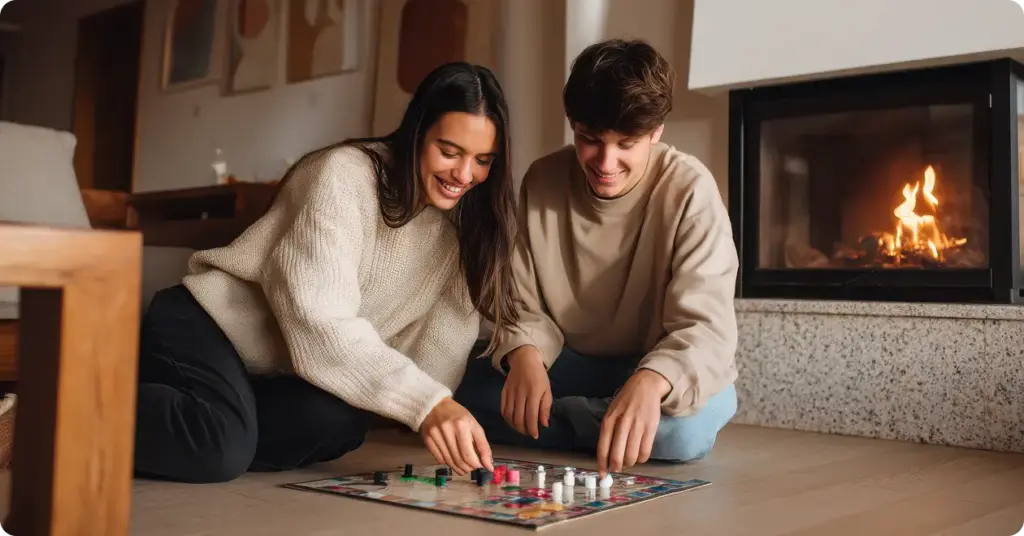 Een jong stel zit op de vloer voor de open haard en speelt een bordspel.